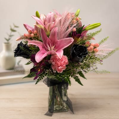 Pink lilies and roses arranged in a glass vase with black ribbon