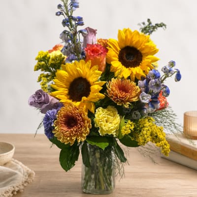 Mixed bouquet with sunflowers, chrysanthemums, and blue flowers in a glass vase