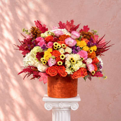 Large mixed bouquet in an orange vase on a white pedestal