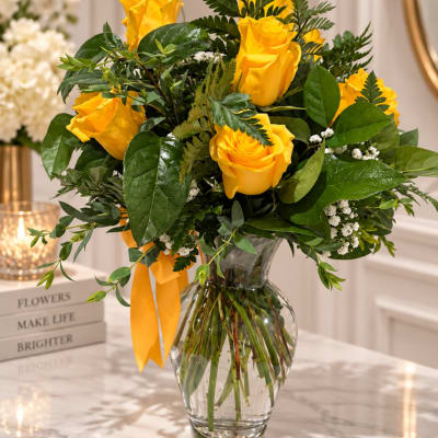 Yellow roses in a clear glass vase with a yellow ribbon