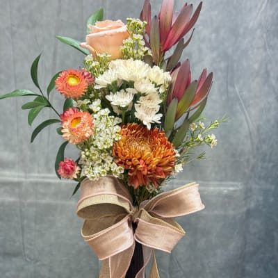 Mixed bouquet with peach rose, white chrysanthemums, and orange blooms tied with a large ribbon