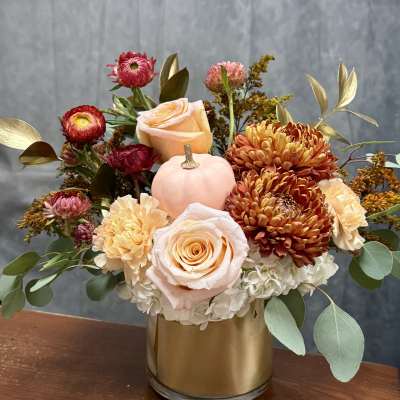 Mixed bouquet in a gold vase with roses, chrysanthemums, and a small pink pumpkin