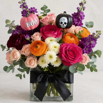 Halloween bouquet in a glass vase with roses, ranunculus, and purple blooms