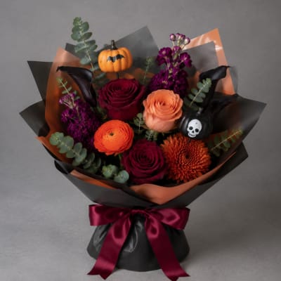 Bouquet of roses, ranunculus, and purple blooms with Halloween pumpkin picks