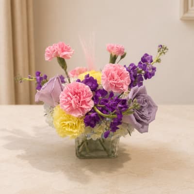 Pink and purple flowers arranged in a square glass vase
