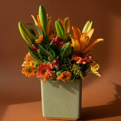 Orange lilies and mixed orange flowers in a ribbed rectangular vase