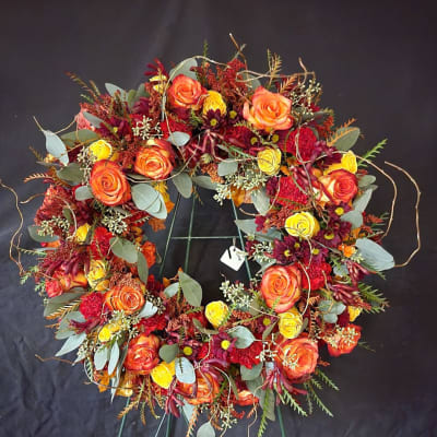 Circular floral wreath with orange and yellow roses on a black stand