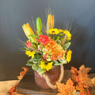Autumn floral arrangement in a rope-wrapped vase with yellow blooms and orange lilies