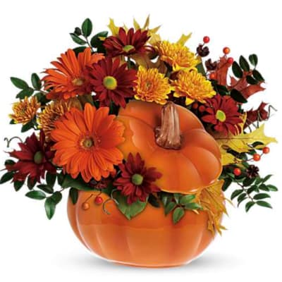 Autumn floral arrangement in a pumpkin-shaped container with orange and burgundy blooms