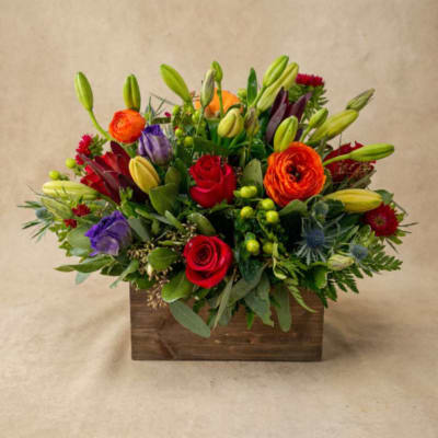 Mixed bouquet in a wooden box with roses, lilies, and bright accent flowers