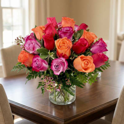 Bouquet of orange, pink, and red roses in a clear glass vase