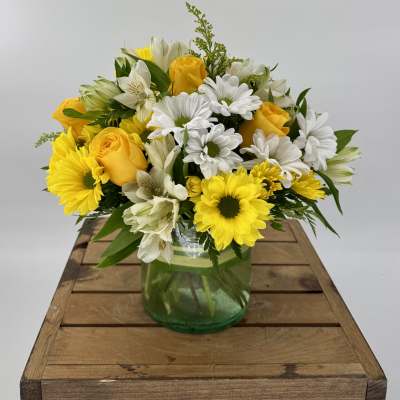 Yellow roses and white daisies arranged in a green glass vase
