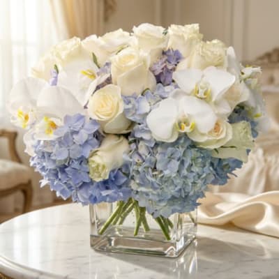 White roses and orchids with blue hydrangeas in a clear square vase