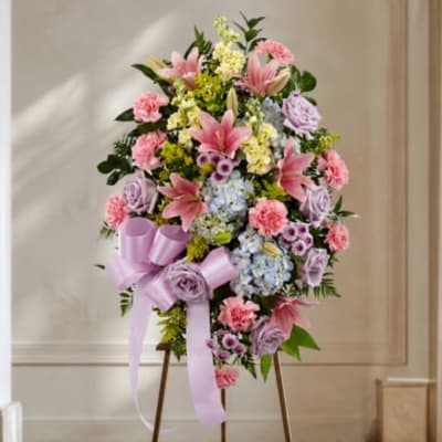 Standing floral spray with pink lilies, carnations, and pastel blooms on a lavender ribboned easel