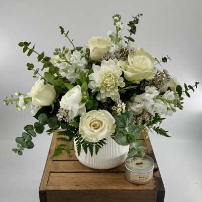 White rose and dahlia arrangement in a ribbed white vase with a small candle