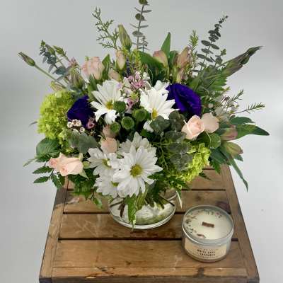 Mixed bouquet in a glass vase with white daisies, pale pink roses, and a candle beside it