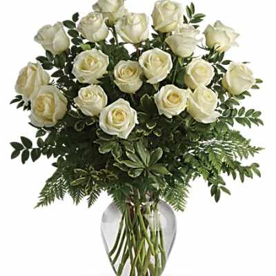 White roses arranged in a clear glass vase with greenery