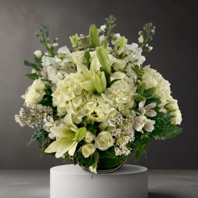 White floral arrangement with lilies, roses, and hydrangeas in a low vase