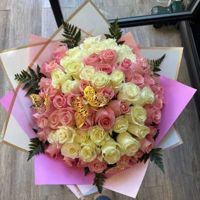 Large round bouquet of cream and pink roses wrapped in layered pink and white paper with gold butterflies.