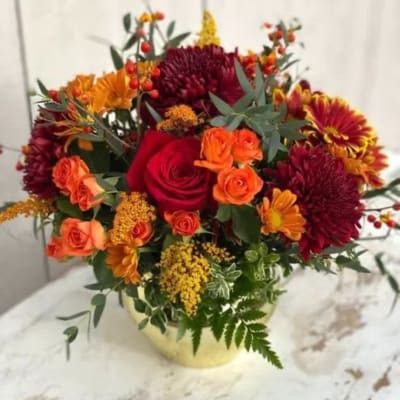 Bouquet of red and orange flowers in a pale vase