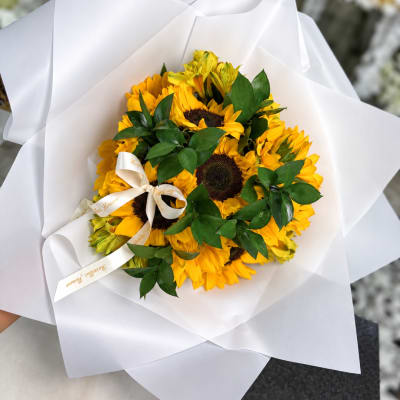 Bouquet of yellow sunflowers wrapped in white paper with a ribbon