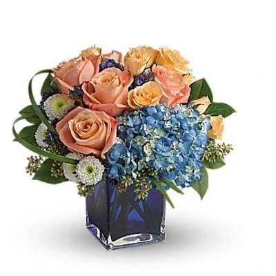 Peach roses and blue hydrangeas in a square glass vase