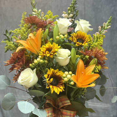 Mixed bouquet with white roses, sunflowers, orange lilies, and a plaid ribbon in a glass vase