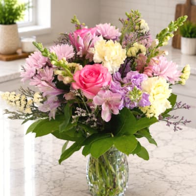 Mixed pink, purple, and cream flowers in a clear glass vase