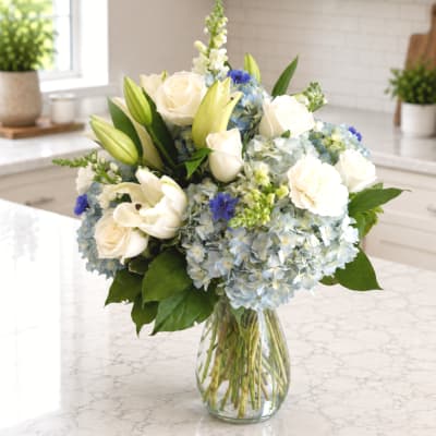 White roses and lilies with blue hydrangeas in a glass vase