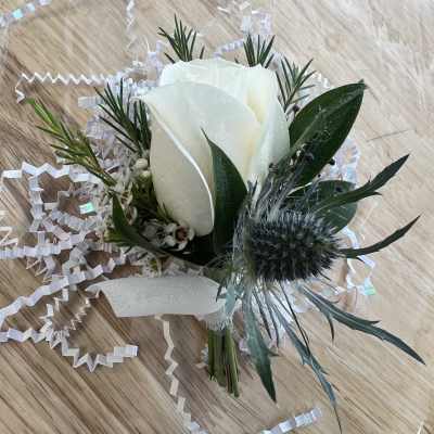 White rose boutonniere with greenery and ribbon on a wood surface