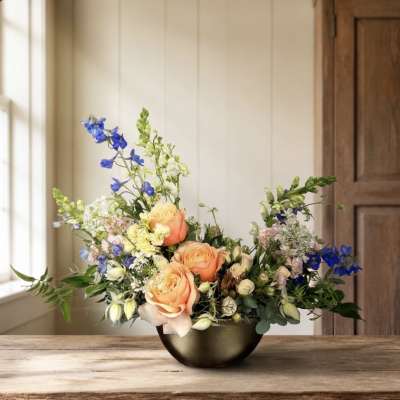 Peach roses and blue flowers arranged in a dark bowl vase