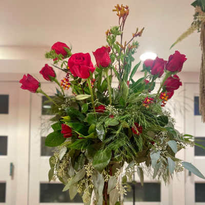 Tall vase arrangement of red roses with mixed greenery