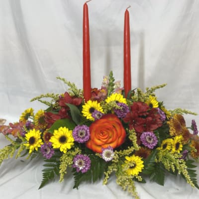 Floral centerpiece with two red taper candles and mixed blooms in a low arrangement