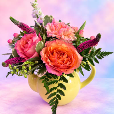 Pink and orange flower arrangement in a yellow mug-shaped vase
