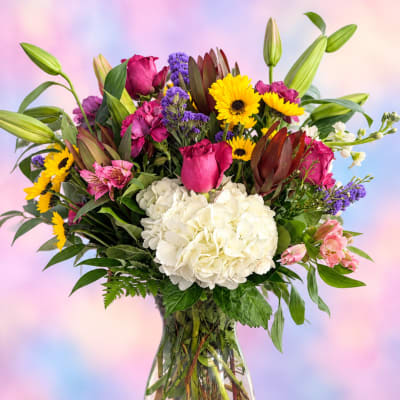 Mixed bouquet with white hydrangea, pink roses, and yellow daisies in a glass vase
