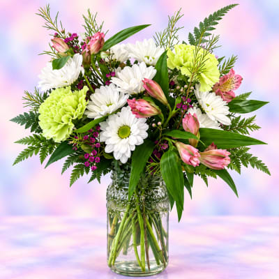 Mixed bouquet of white daisies, pink lilies, and green carnations in a glass jar vase