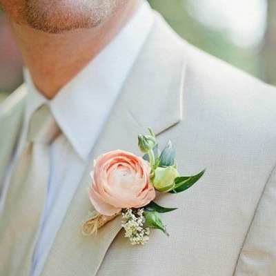 Boutonniere with a blush ranunculus on a beige suit lapel