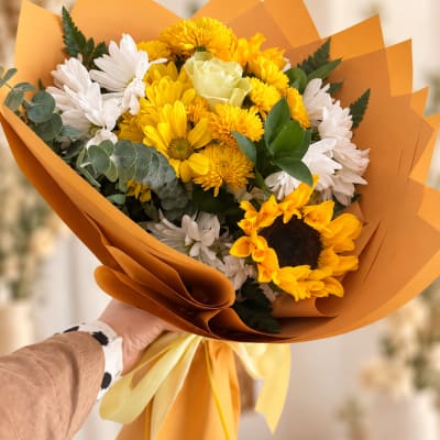 Handheld bouquet of yellow and white flowers wrapped in orange paper