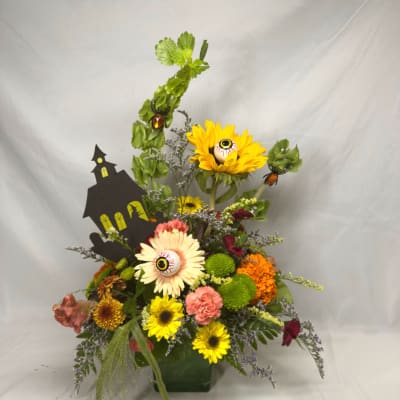 Halloween floral arrangement with sunflowers, mums, and eyeball picks in a green container