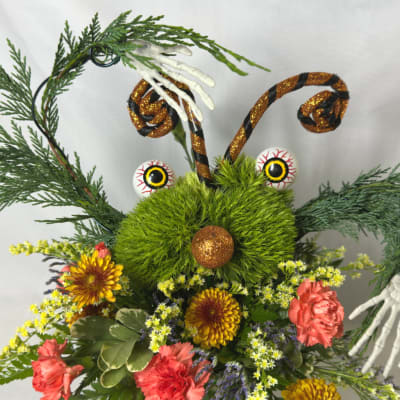 Halloween floral arrangement with a green fuzzy face, glittery antennae, and flowers