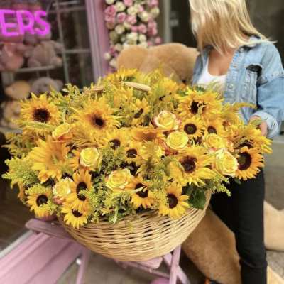 Large basket of yellow sunflowers and roses being held by a woman