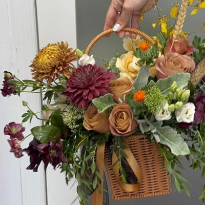 Mixed floral arrangement in a wicker basket with a handle and ribbon