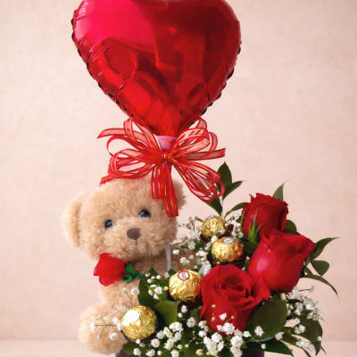 Teddy bear gift arrangement with red roses, chocolates, and a heart balloon