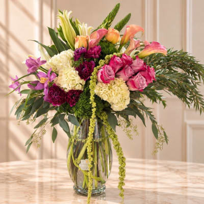 Mixed bouquet of pink roses, lilies, hydrangeas, and calla lilies in a glass vase