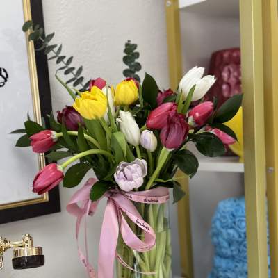 Bouquet of pink, yellow, and white tulips in a glass vase with a pink ribbon