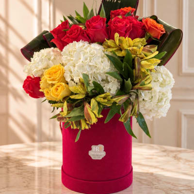 Red and yellow roses with white hydrangeas in a pink hat box
