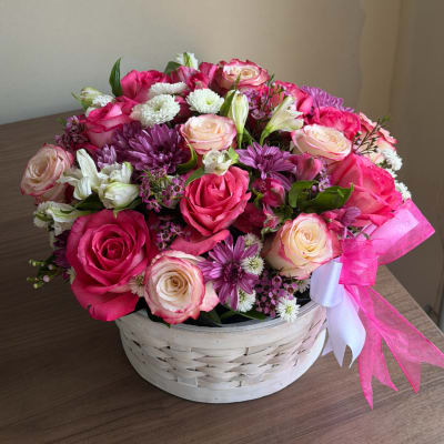 Pink and white rose bouquet in a white basket with a pink ribbon