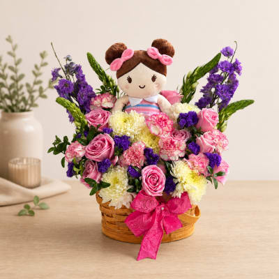 Basket arrangement with a doll surrounded by pink, purple, and white flowers