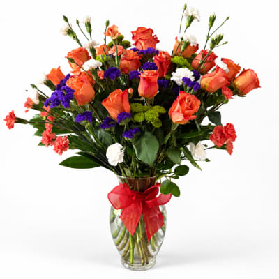 Bouquet of orange roses, purple statice, and white carnations in a glass vase