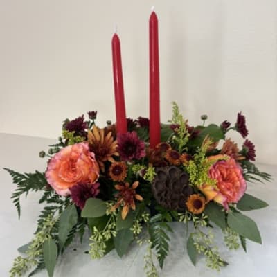 Low floral centerpiece with two red taper candles and peach-orange blooms